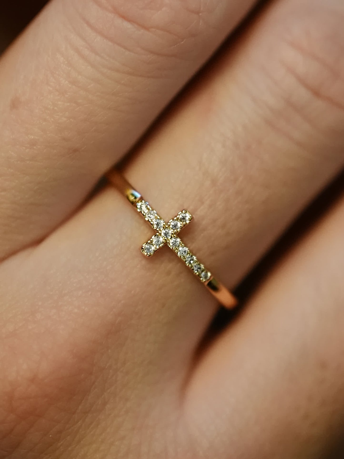 The dainty gold cross ring worn on a woman’s hand, highlighting its minimalist, faith-inspired design