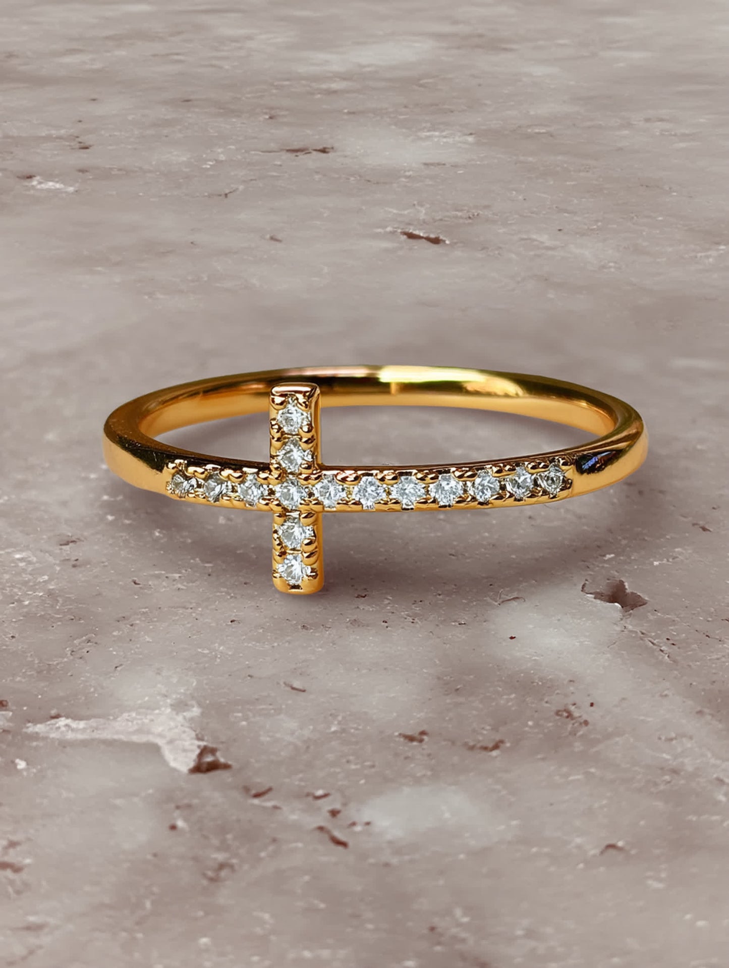 Close-up of the gold cross ring resting on a marble surface, showcasing the sparkle of its crystal-inlaid cross