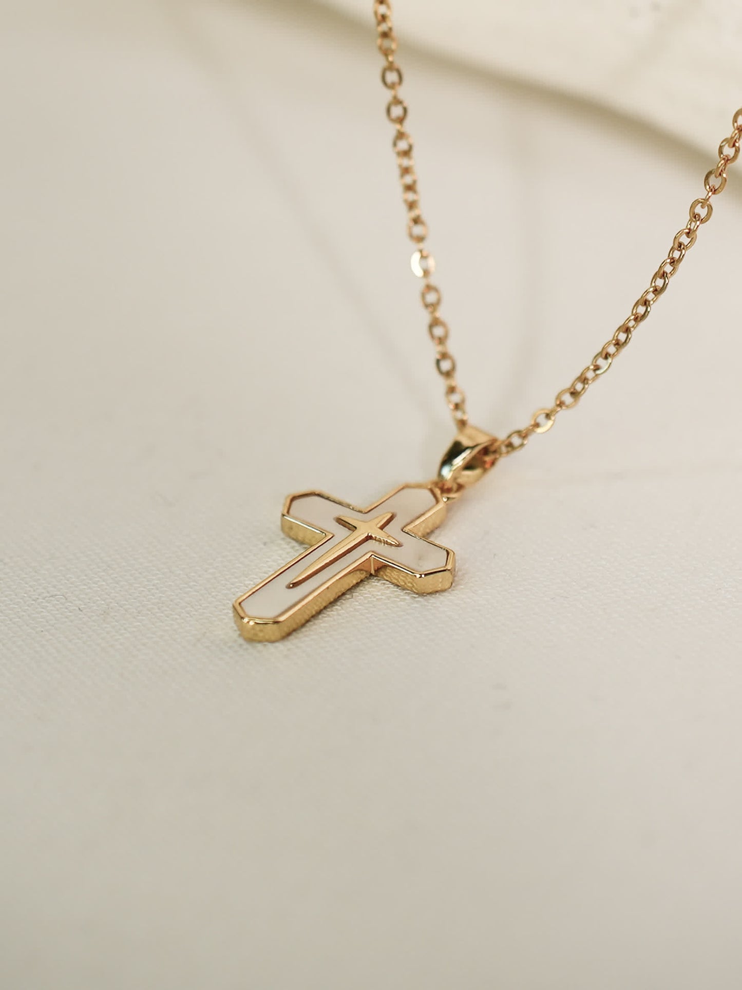 Tilted flat-lay view of the white enamel cross necklace placed on light fabric