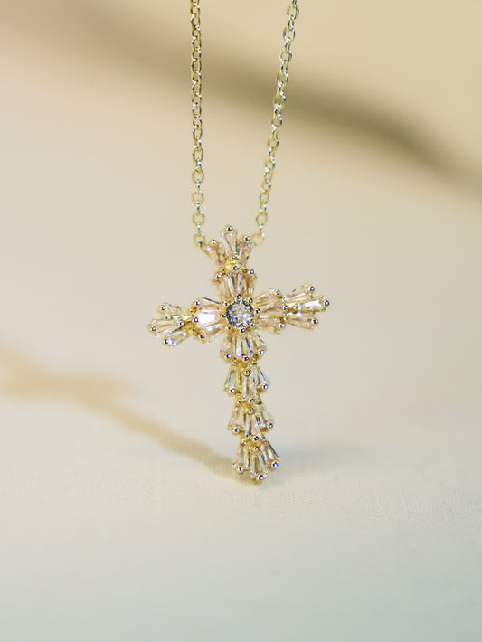 Gold crystal flower cross necklace suspended mid-air against a soft neutral background, highlighting its radiant silhouette