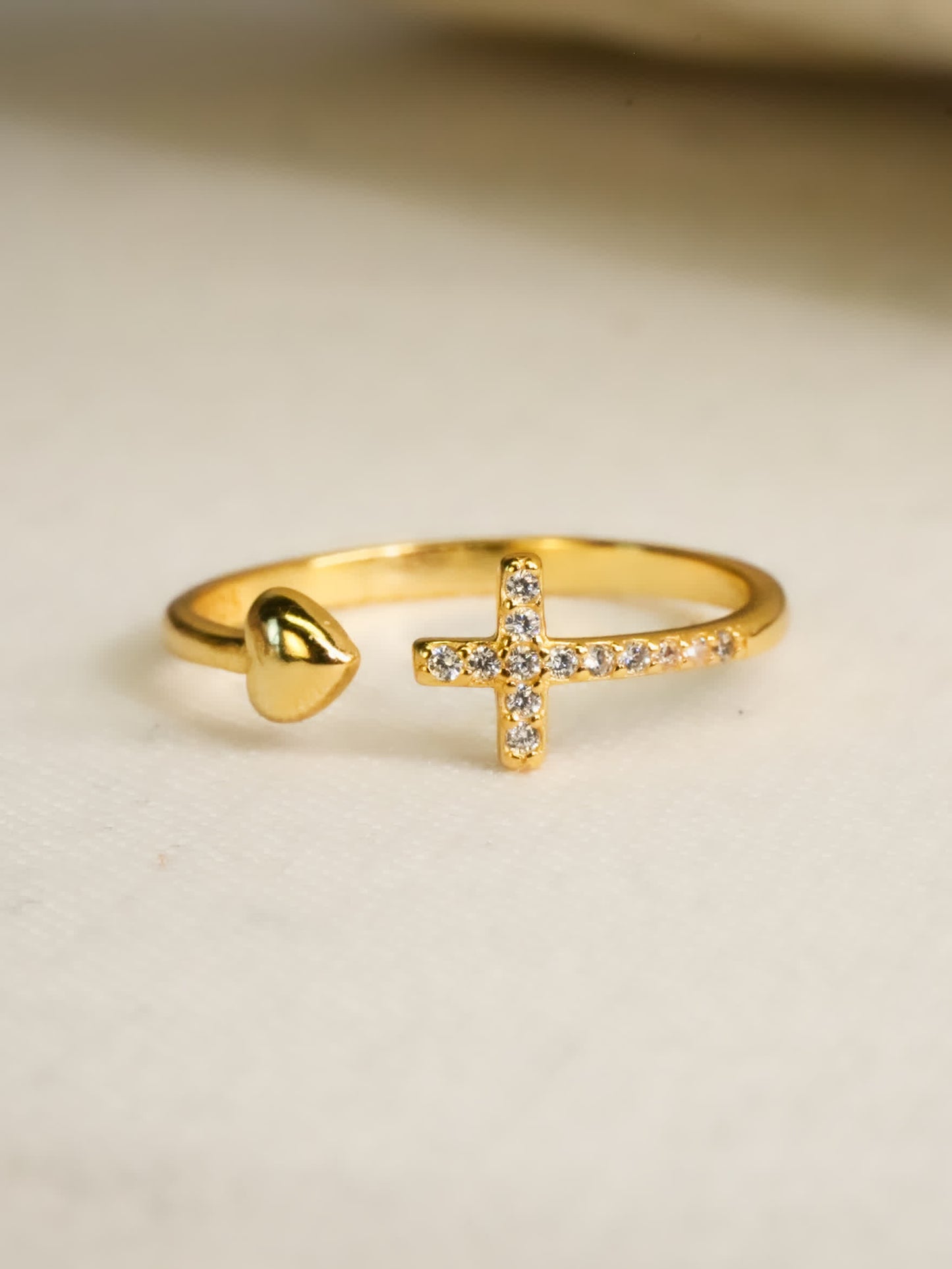 Gold ring with a heart and cross design on a beige background