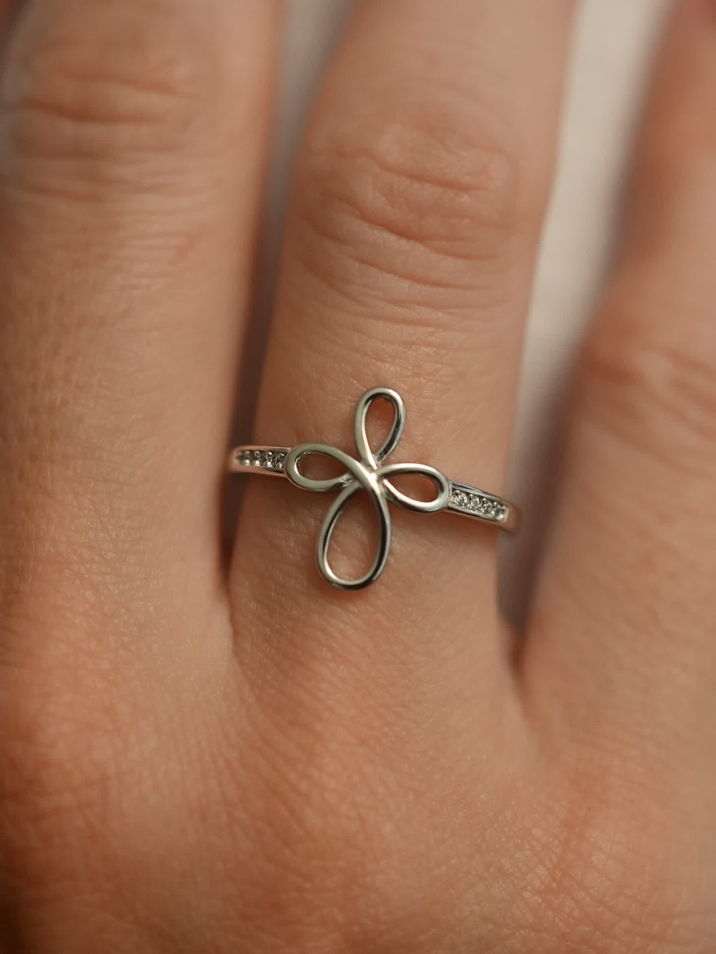 Softly lit close-up of the ring on a beige surface, showcasing the feminine silver cross with open petal design