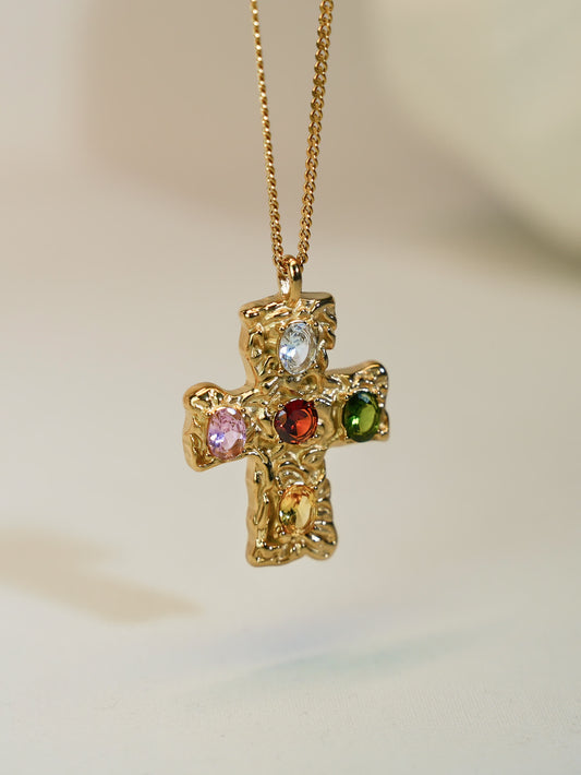 Close-up of hammered gold cross pendant with five colorful zircon gemstones on neutral background