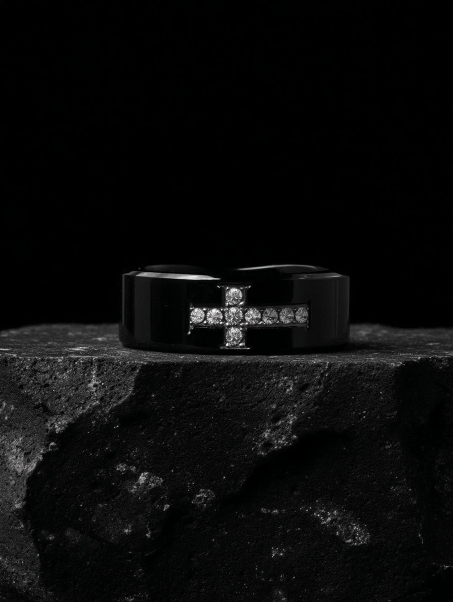 Angled view of Creed Noir Black Cross Ring displayed on rugged stone surface, capturing the masculine design and glossy black finish.