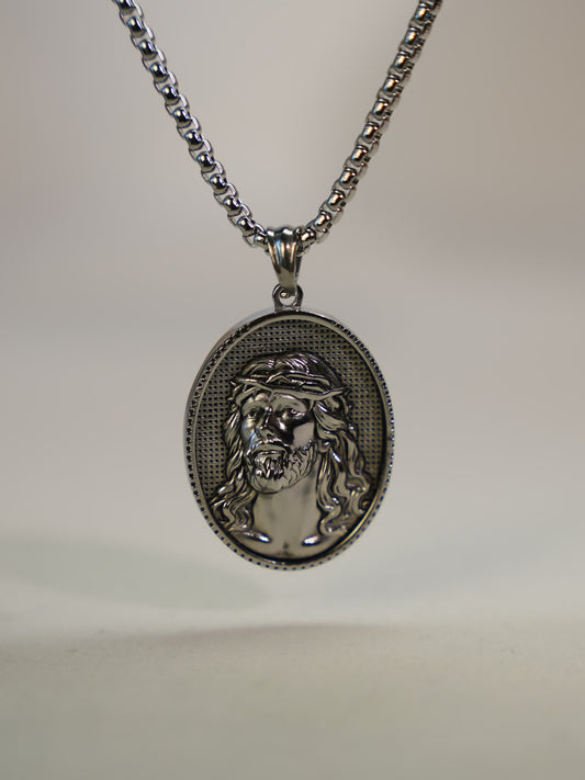 Close-up of oxidized silver Jesus pendant necklace resting upright on a soft neutral surface, highlighting the intricate sculpted detail.