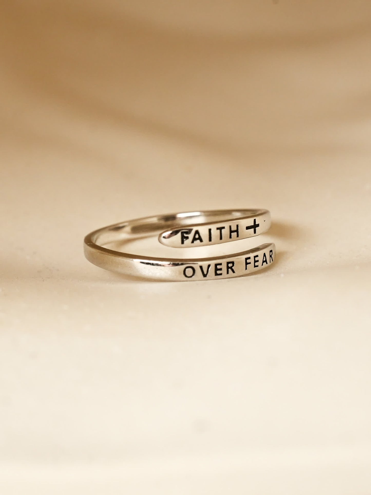 Sterling silver faith over fear ring wrapped around finger, highlighting engraved Christian words in black