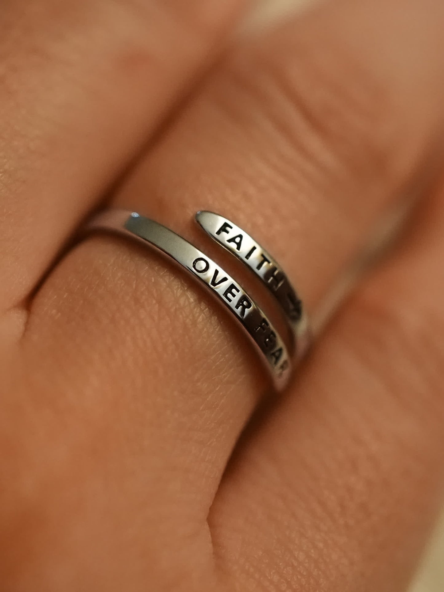 Silver ring with 'FAITH OVER FEAR' engraving on a finger