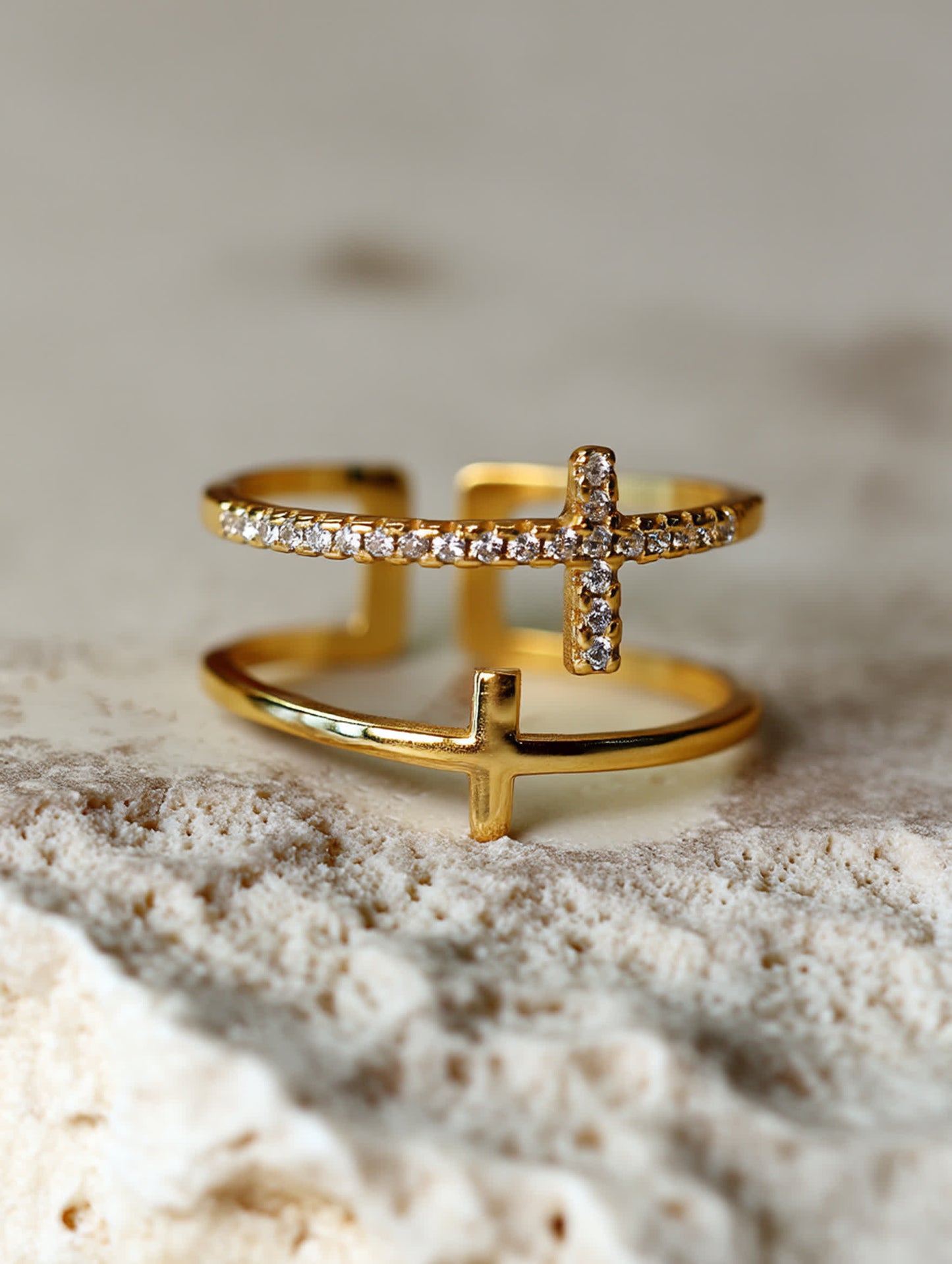 Minimalist photo of the double cross ring against a soft white fabric background, emphasizing the polished 18K gold tone and delicate craftsmanship