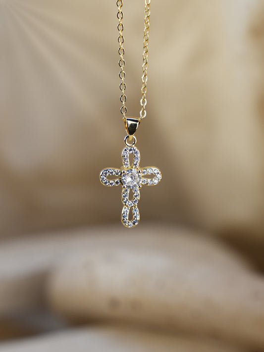 Gold interlocking cross pendant hanging in front of soft neutral background