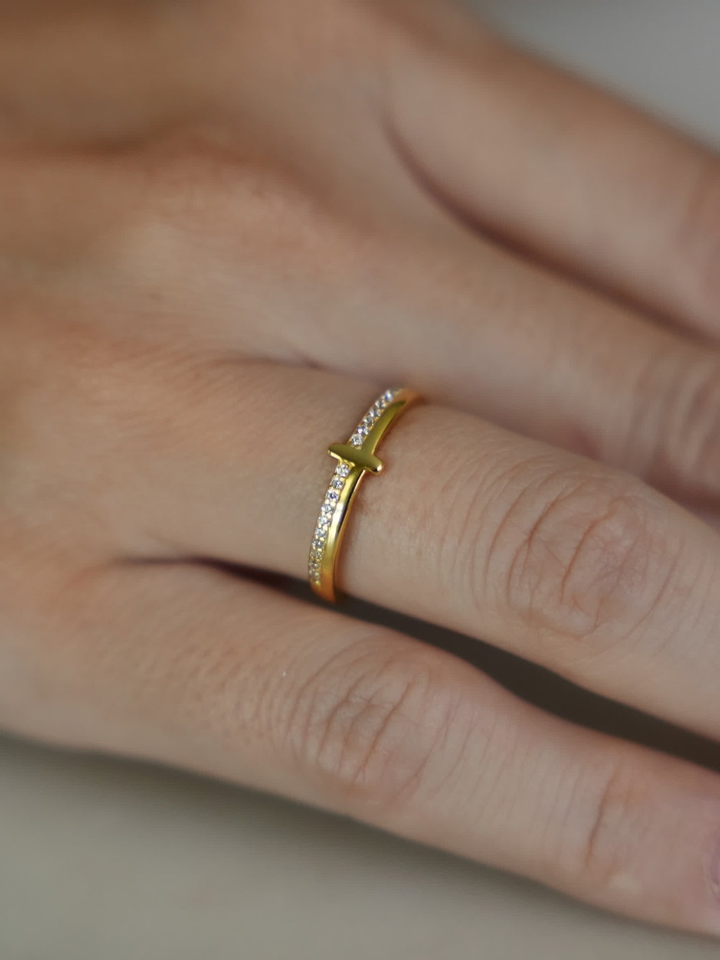 Woman’s hand wearing thin gold cross ring with sideways cross design