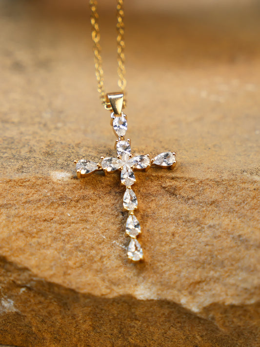 Close-up of the gold crystal cross necklace placed on warm stone surface, highlighting sparkle and texture