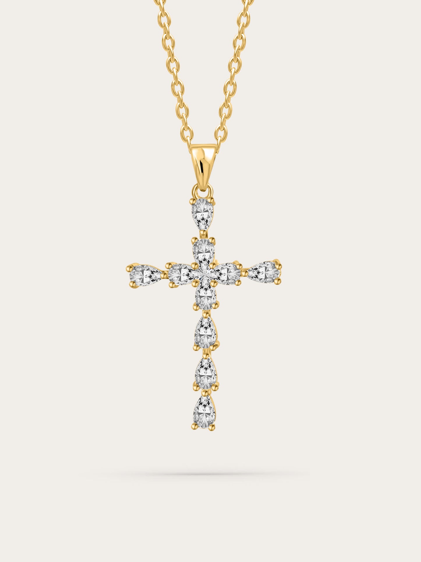 Studio shot of elegant gold cross necklace with teardrop zircon crystals on soft beige background