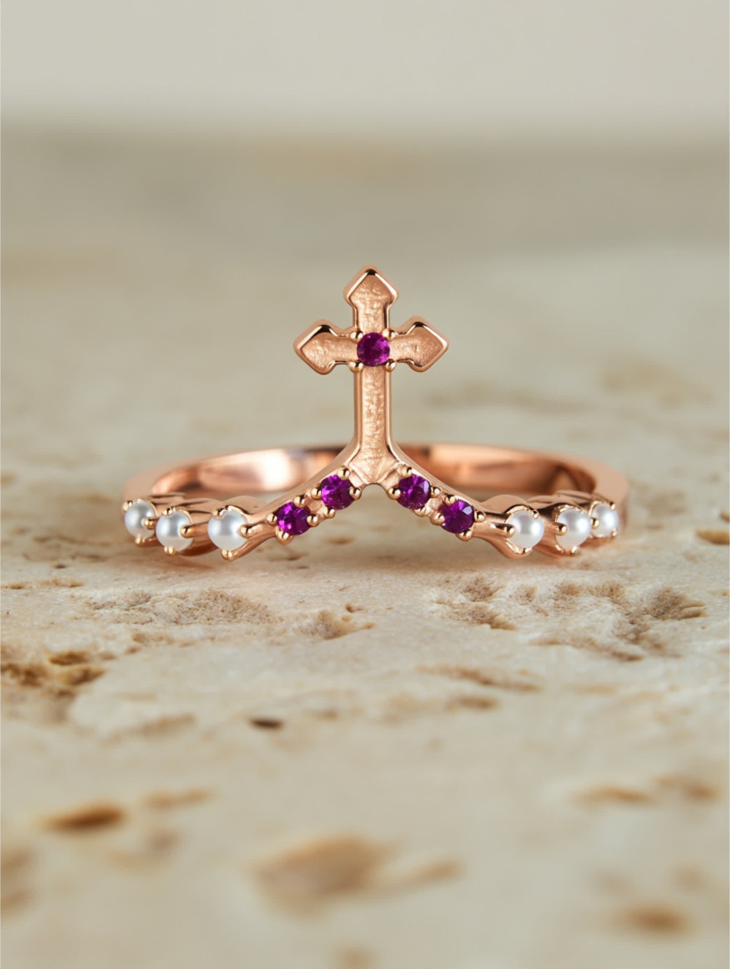 Front-facing photo of pink and white crystal cross ring on textured beige slab