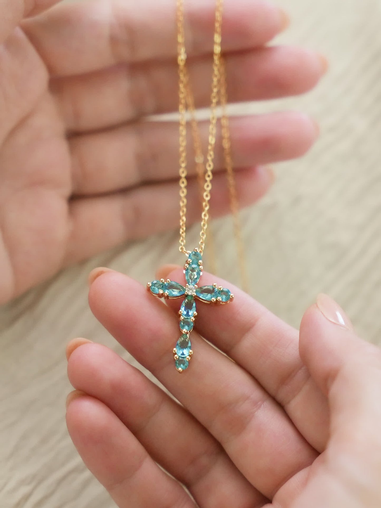 Hand holding the feminine cross pendant, showcasing scale, crystal details, and soft shine