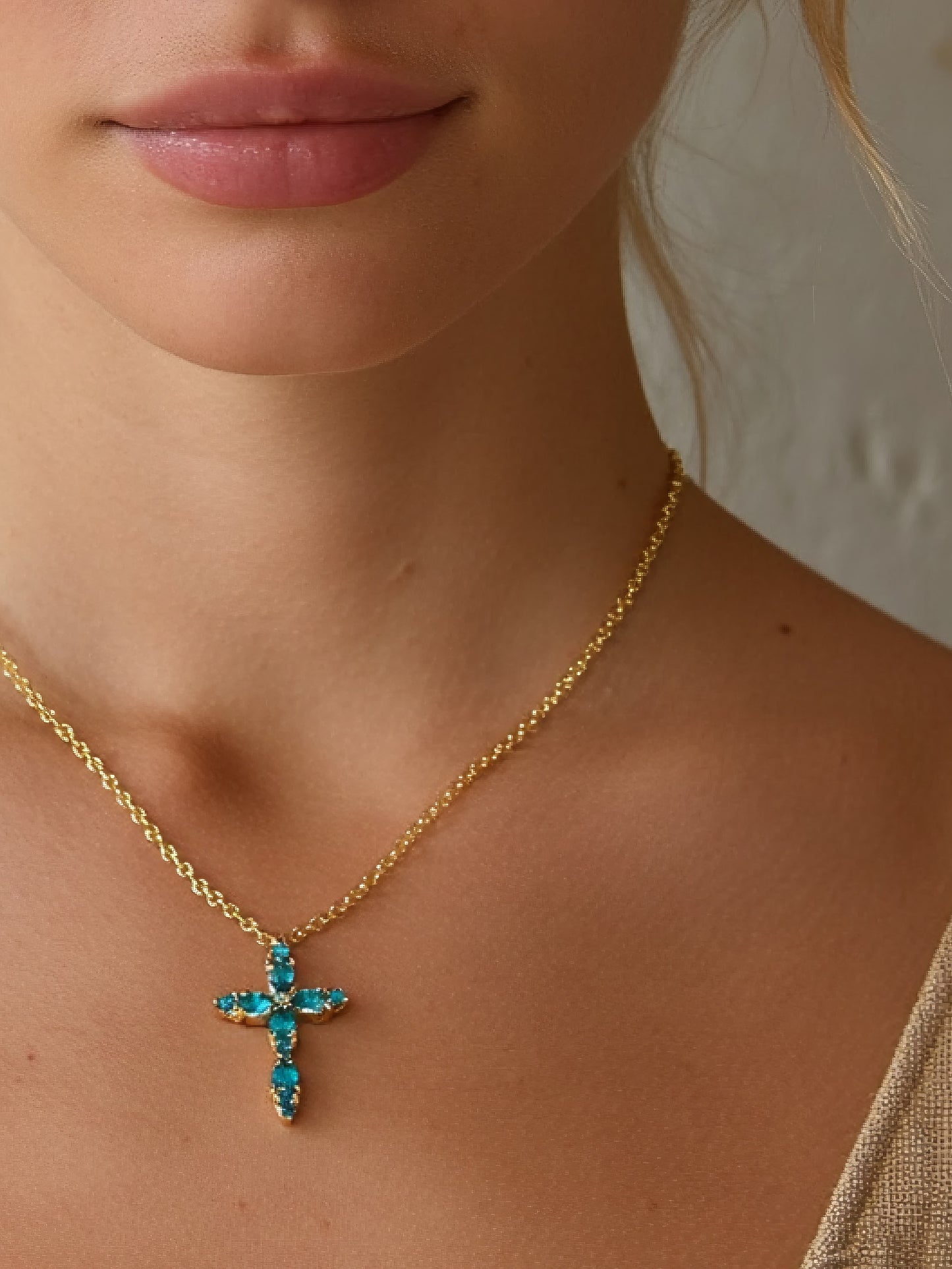 Woman wearing the gold and aquamarine cross necklace, showing its delicate fit and radiant design