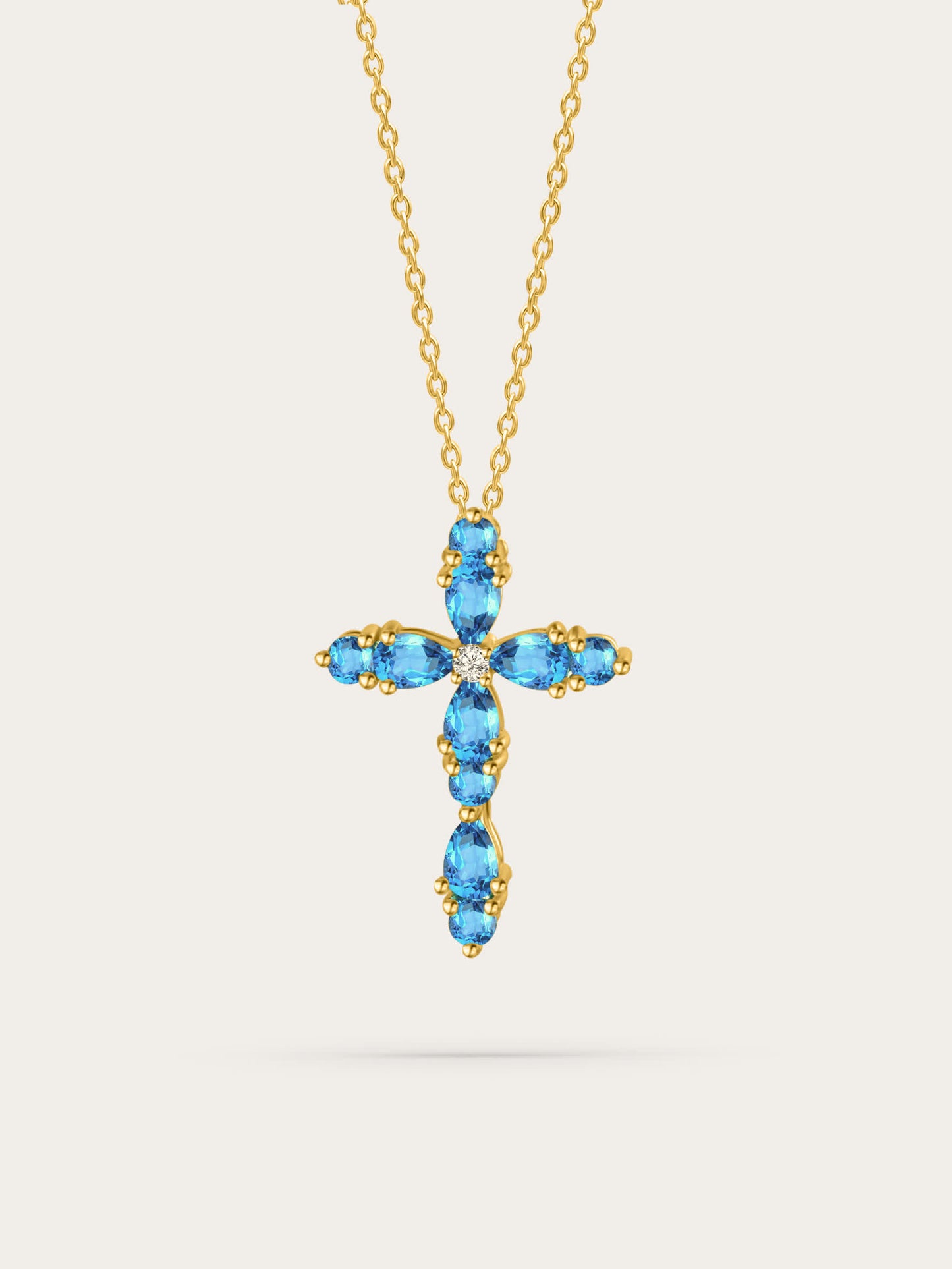 Studio photo of feminine cross pendant with aquamarine zircon stones set in gold, displayed on soft beige background