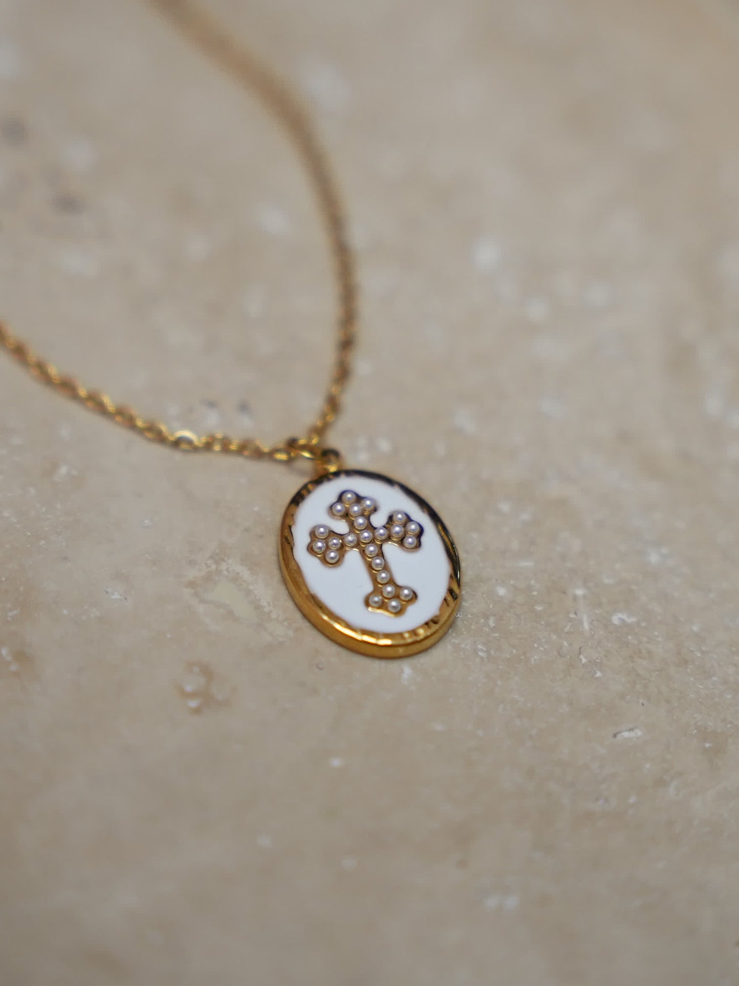 Pendant on warm stone surface
Enamel cross necklace with gold oval pendant resting on natural stone