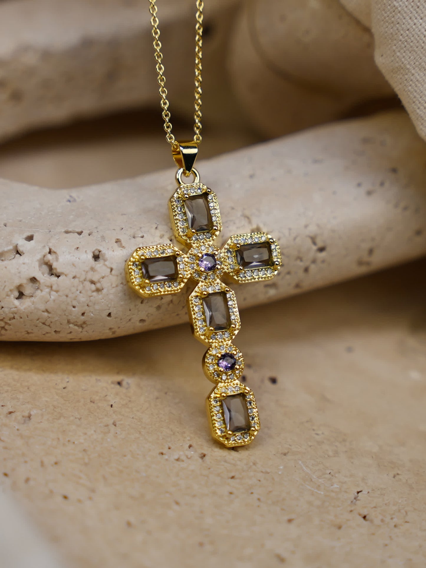 Close-up of the Faithstone Vintage Zircon Cross Necklace resting on textured stone surface, showcasing gold finish and deep-toned zircon crystals