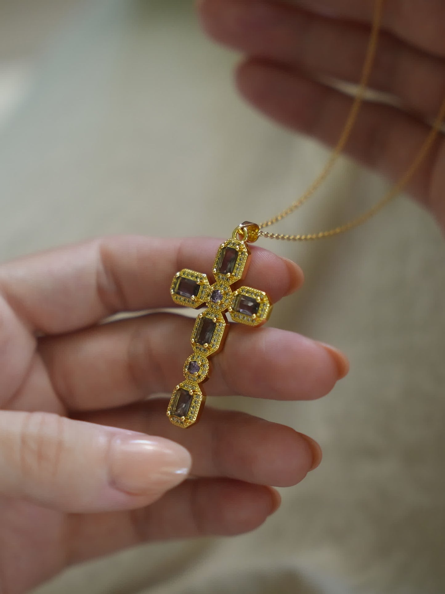 Hand holding the Faithstone gold zircon cross pendant, showing scale and sparkling stone detail