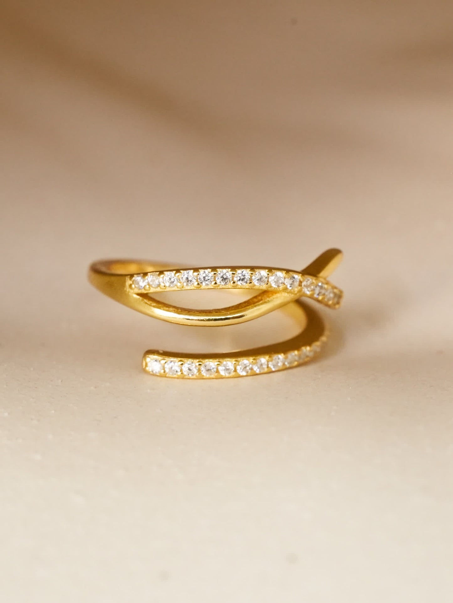 Side view of the gold Ichthys Grace Cross Ring resting on a soft cream surface with natural light