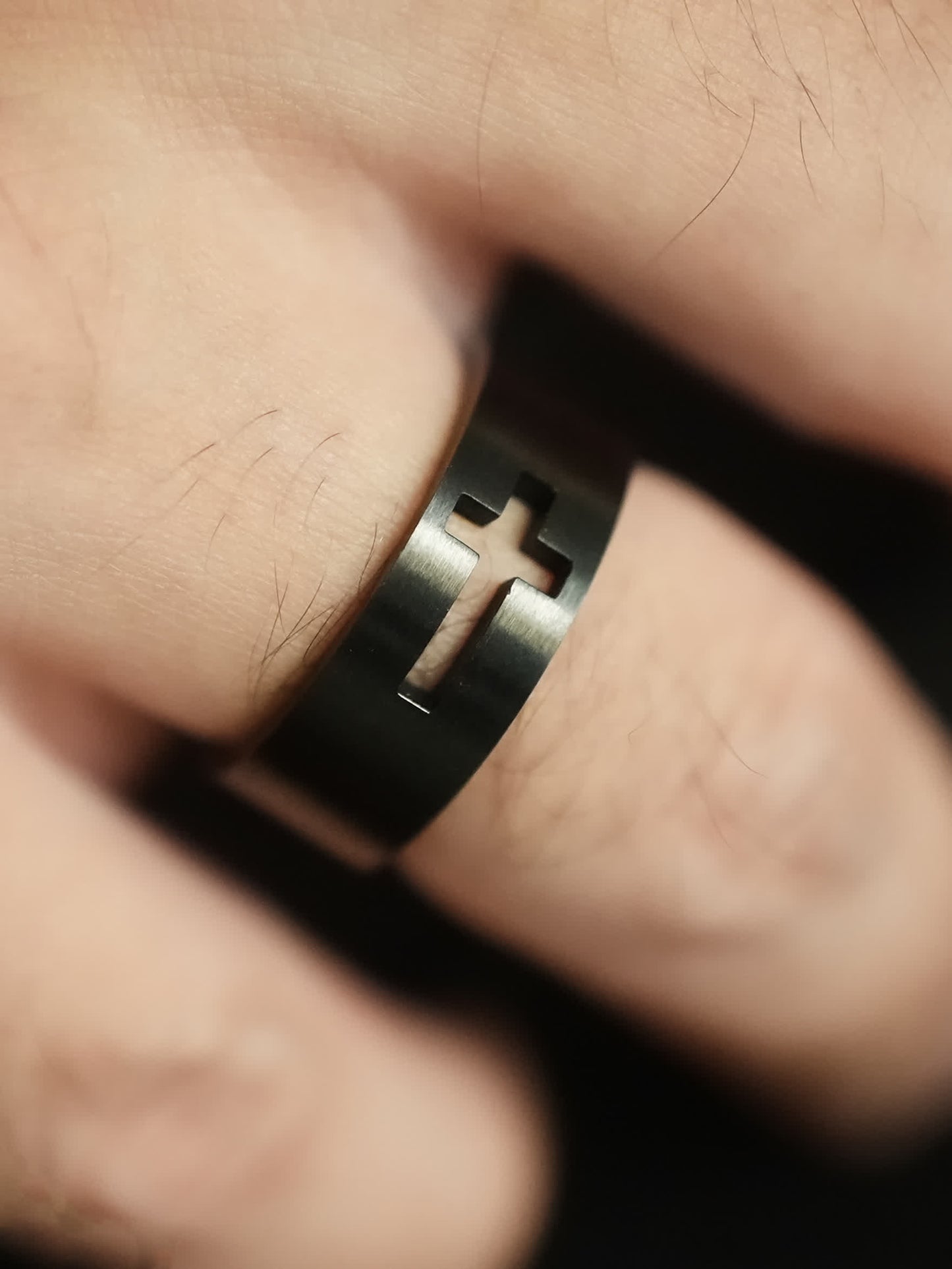 Close-up of the man’s ring on a finger, showcasing the thick black band with a recessed cross cut-out that aligns with the woman’s ring.