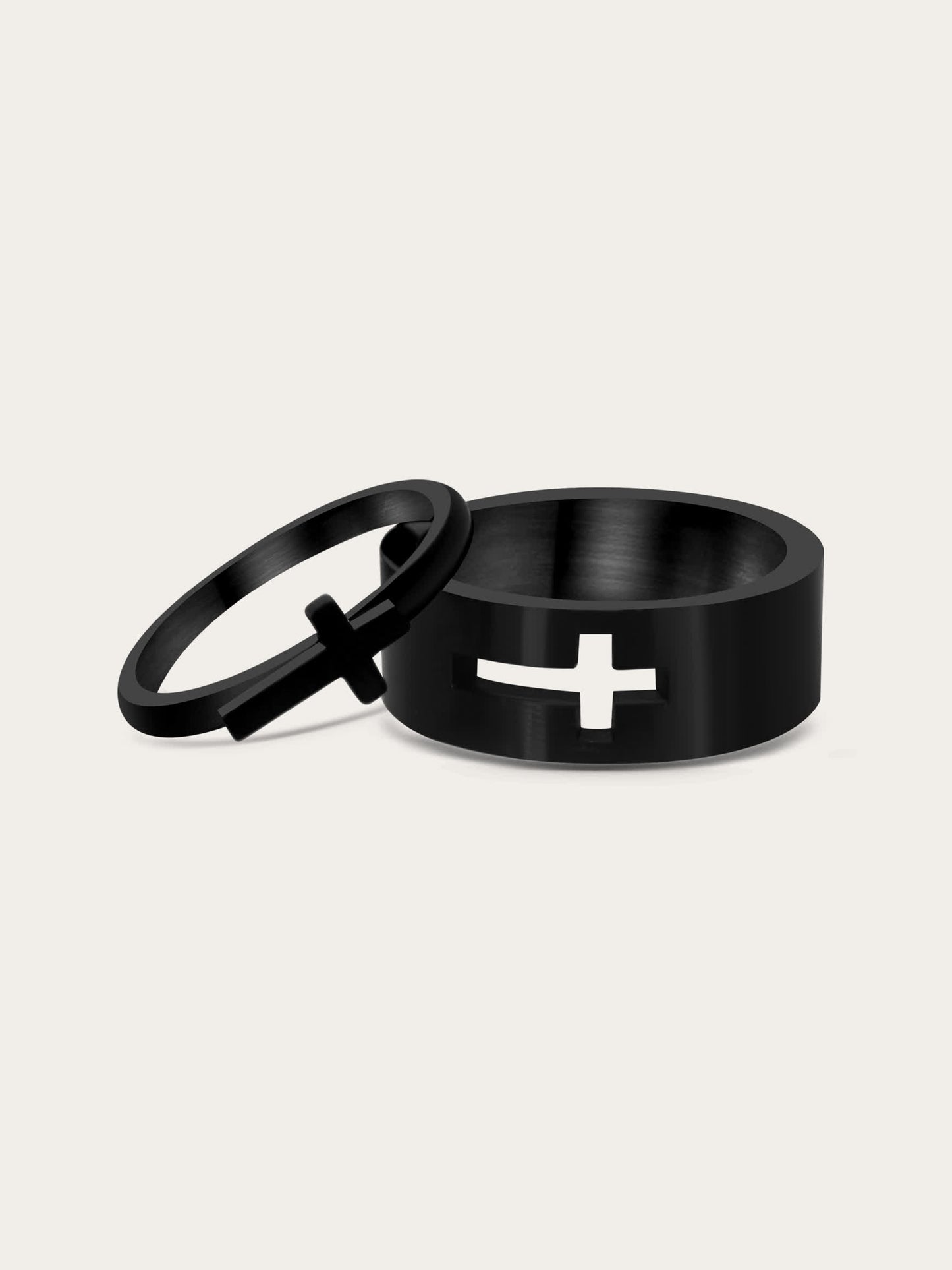 Front-facing studio image of a black stainless steel couple ring set featuring an interlocking cross design — one ring with a raised silver cross and the other with a cross-shaped cut-out.