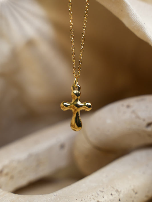 Close-up of the gold sculptural cross pendant resting against curved travertine stone, emphasizing its reflective finish