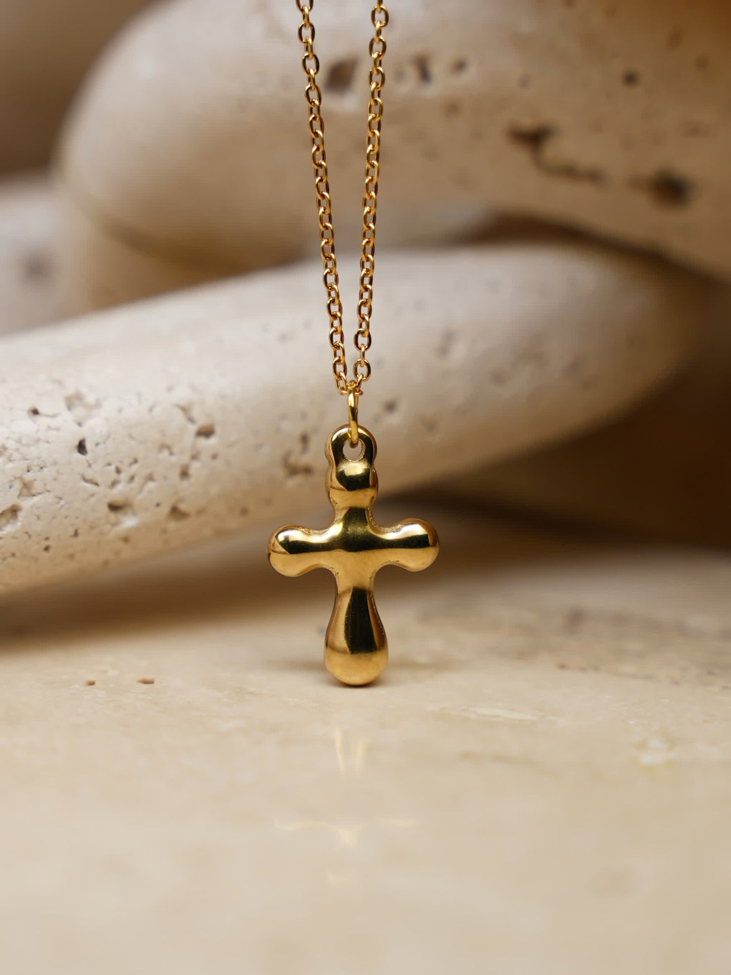 Side view of the molten-style gold cross necklace on natural travertine, capturing texture and organic contours