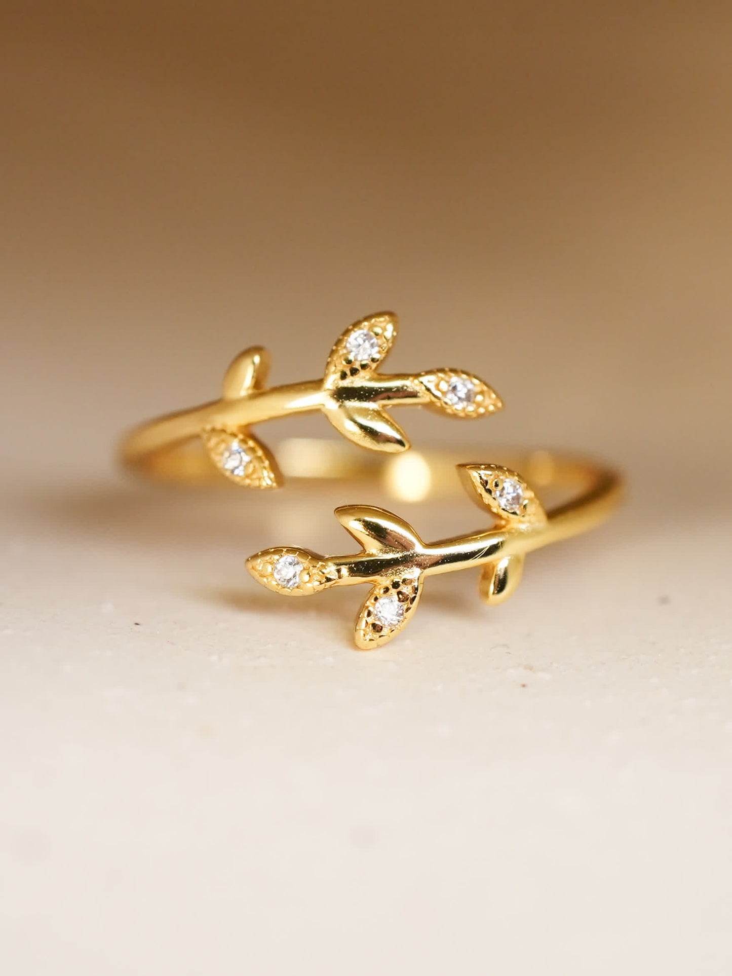 Close-up of gold-plated olive promise ring on cream surface