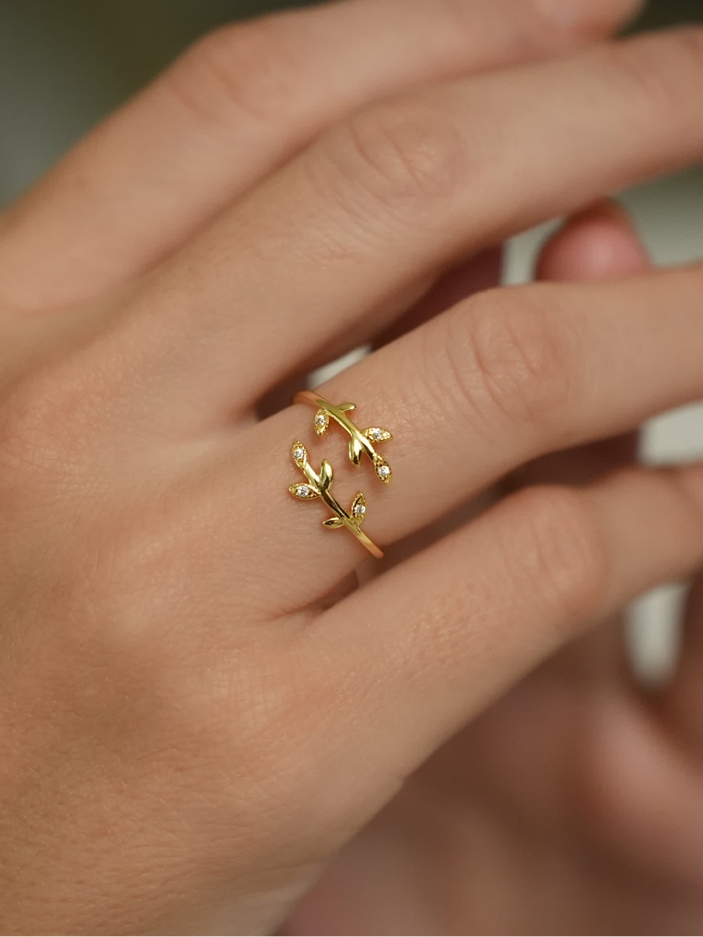 Delicate olive branch ring shown on woman's finger in natural light