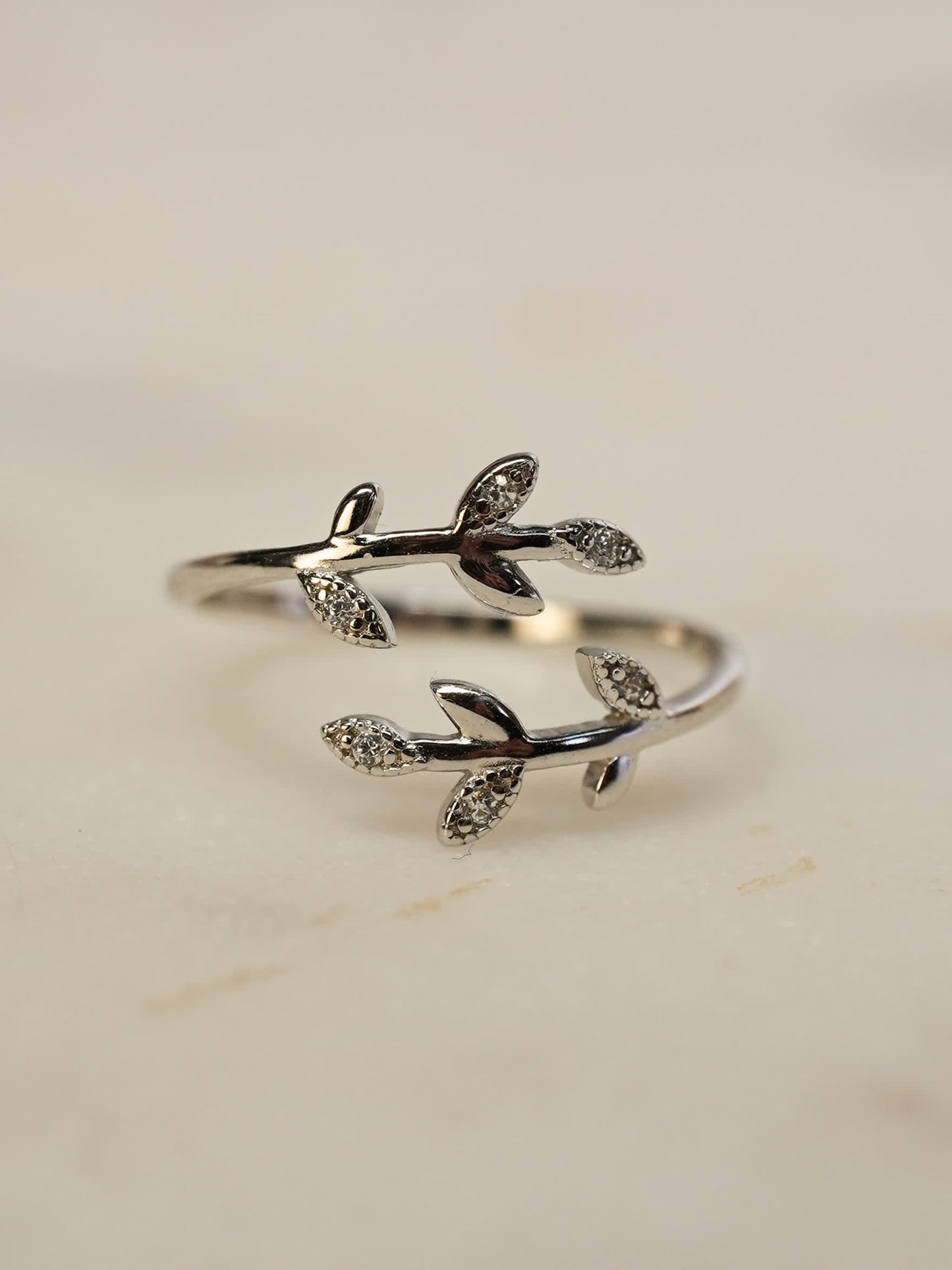Delicate silver olive ring resting on white marble, with glistening zirconia leaves and elegant curves.
