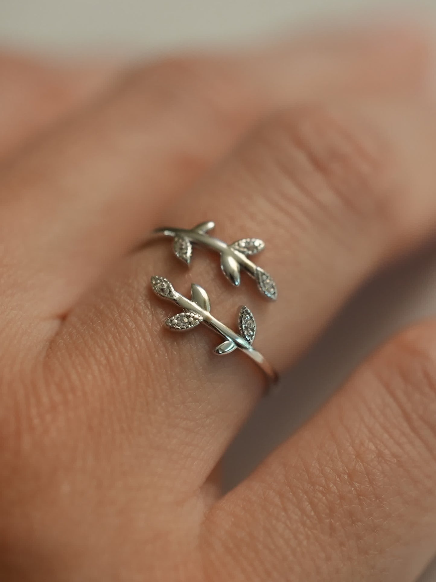 Close-up of a sterling silver olive branch ring worn on a hand, highlighting the graceful wrap-around leaf design.