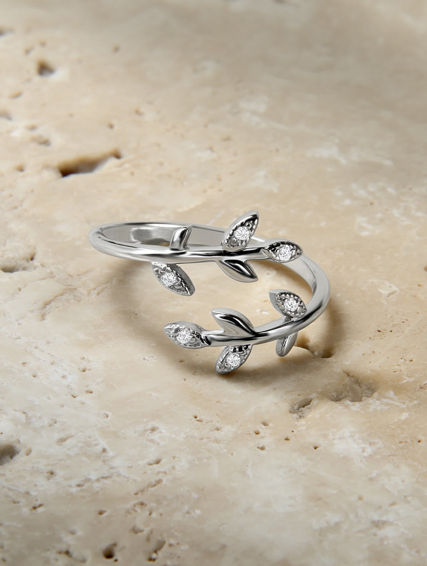 Olive leaf silver ring placed on a natural travertine slab, showcasing its organic shape and shimmering stones.