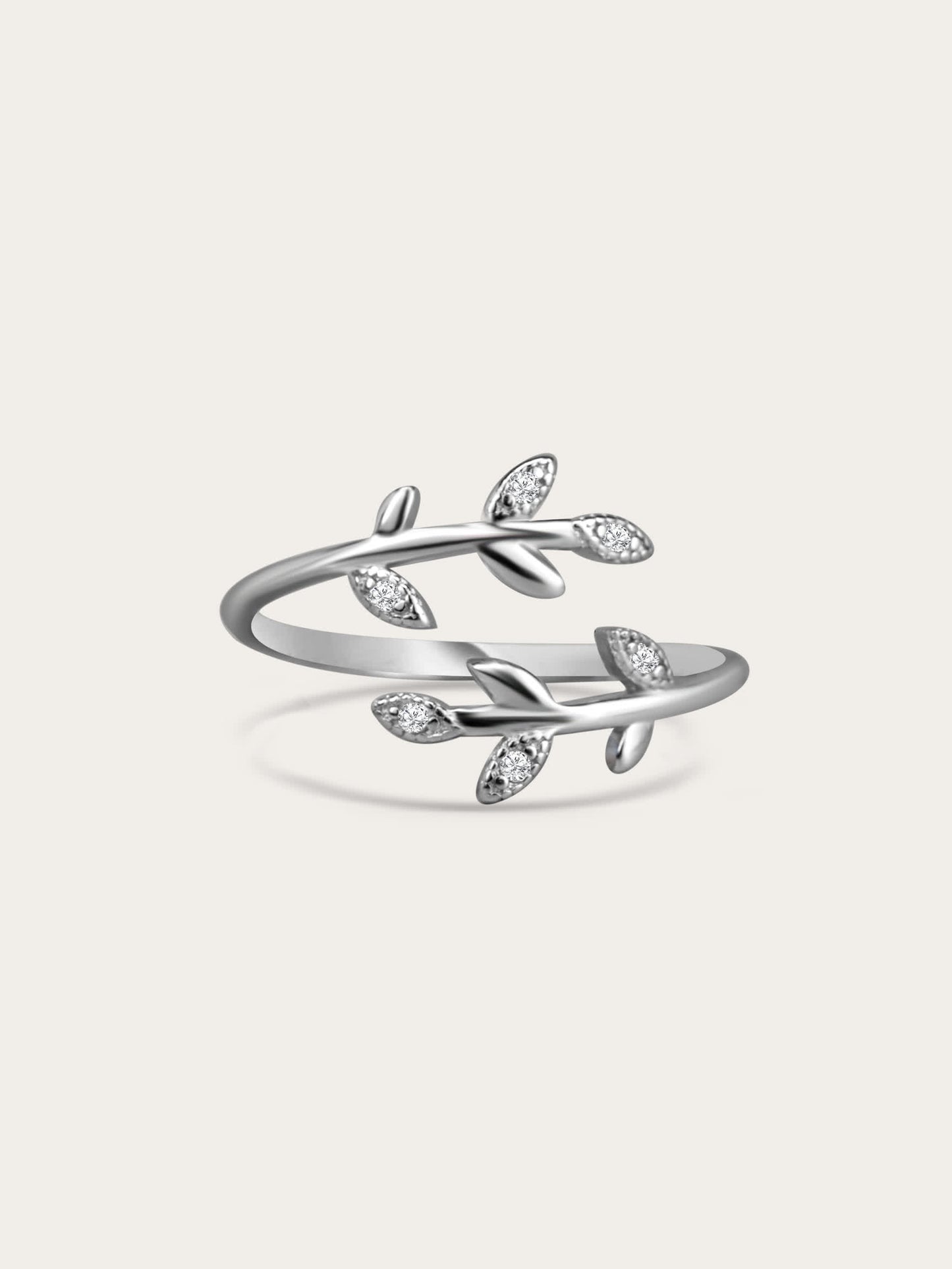 Sterling silver olive branch ring with cubic zirconia leaves on a cream background, minimal studio lighting.