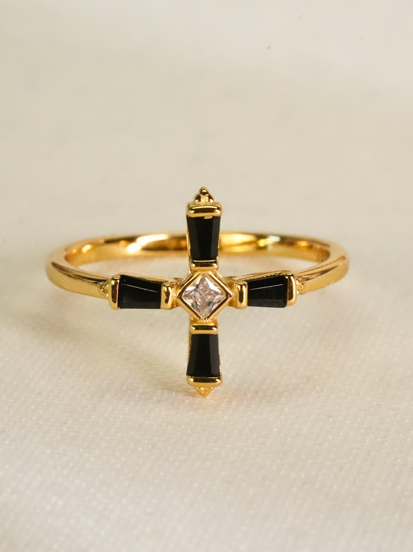 A close-up of the ring laying flat on a soft white textile, capturing the precise geometry and high-polish finish of the cross design.