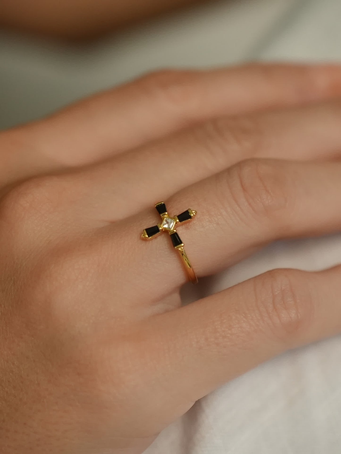 The ring worn on a model’s finger, showcasing its elegant cross design with black baguette stones and a shimmering white center stone.