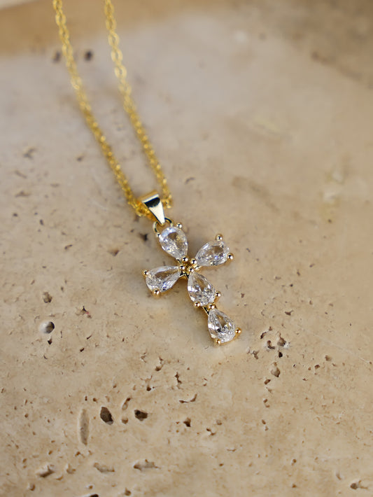 Gold teardrop crystal cross pendant resting on travertine stone surface