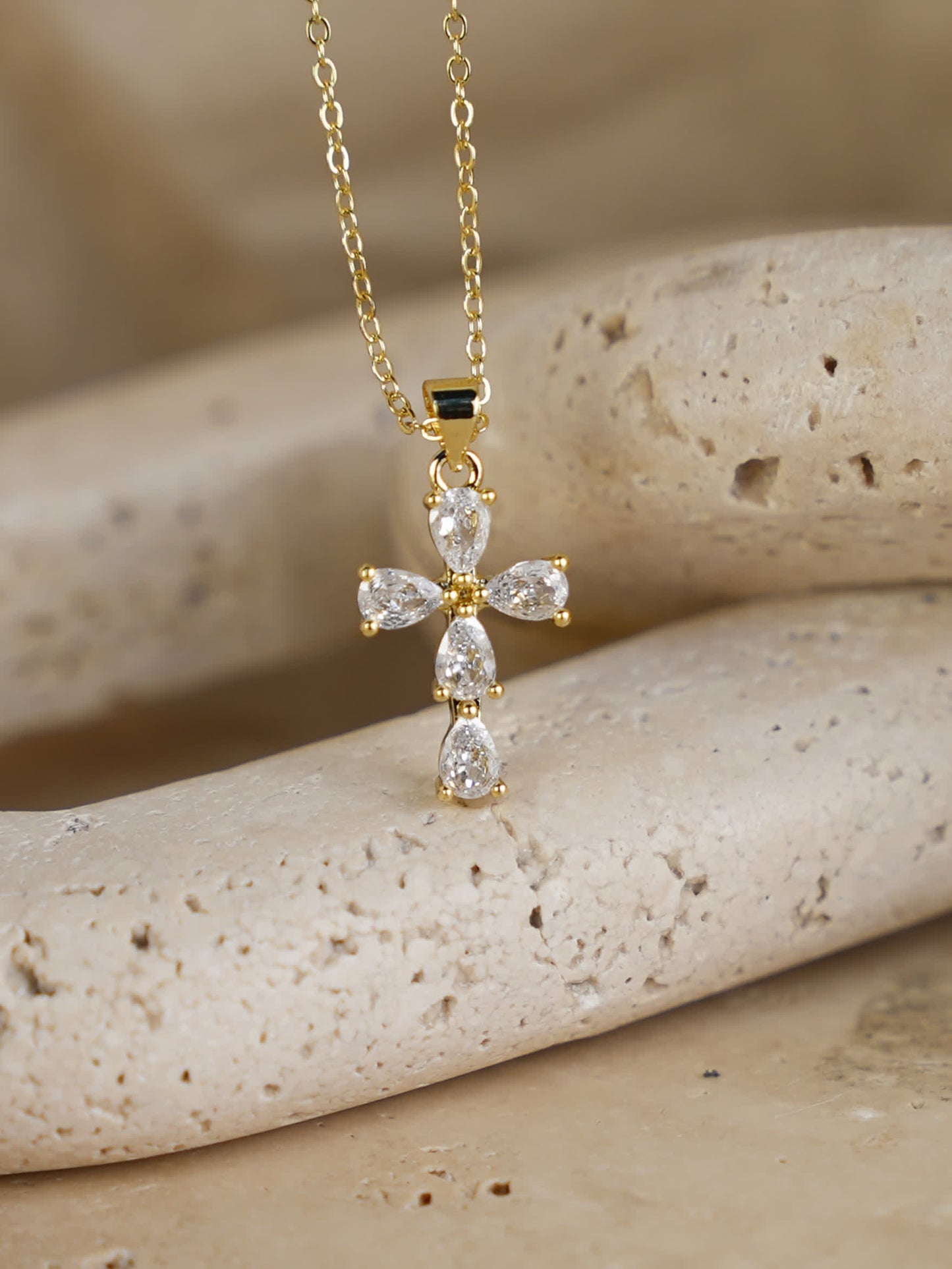 Delicate marquise and pear-cut crystal cross necklace styled on natural stone background