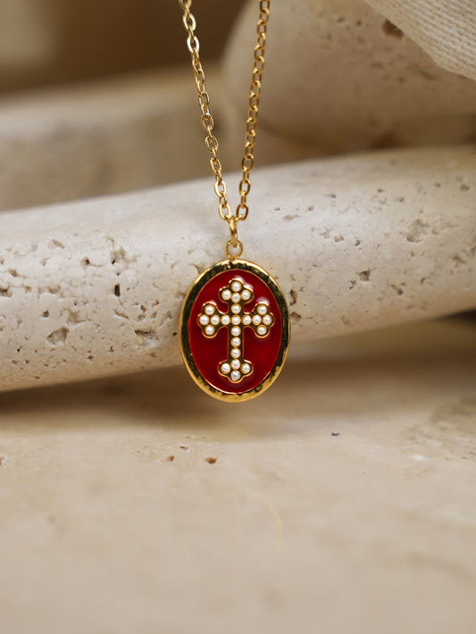 Red and gold enamel cross necklace displayed on curved beige stone