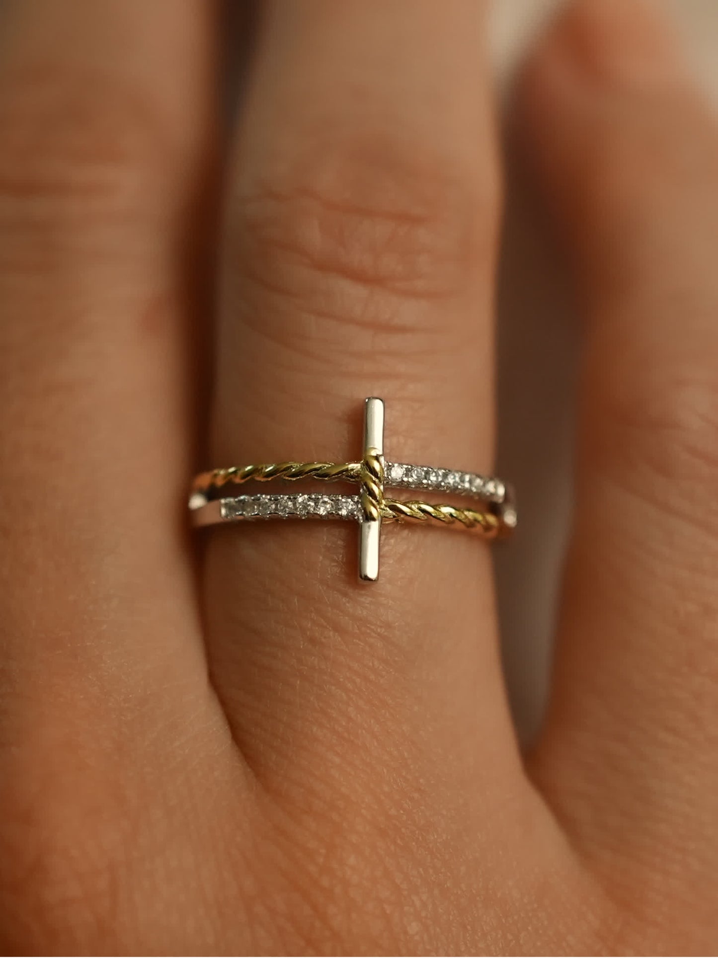 Close-up of two-tone silver and gold cross ring worn on finger, highlighting elegant wrap design and symbolic vertical cross shape