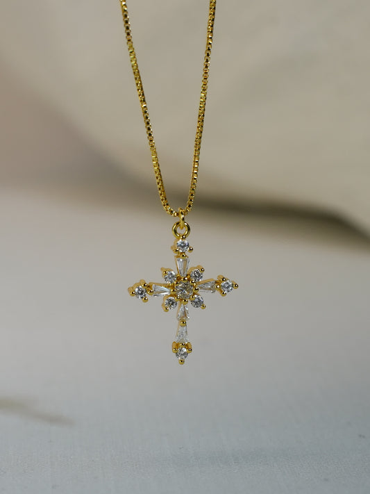 Starburst crystal cross pendant hanging on gold chain, displayed against a minimalist neutral backdrop