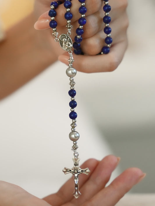 Person holding a lapis lazuli Catholic rosary necklace with silver crucifix pendant