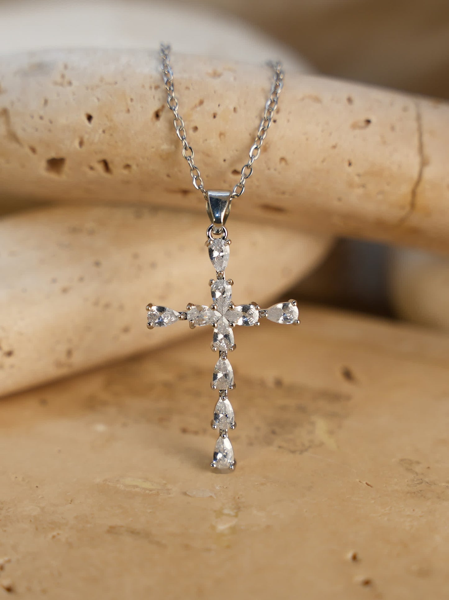 Close-up of the delicate silver cross necklace displayed on natural travertine stone