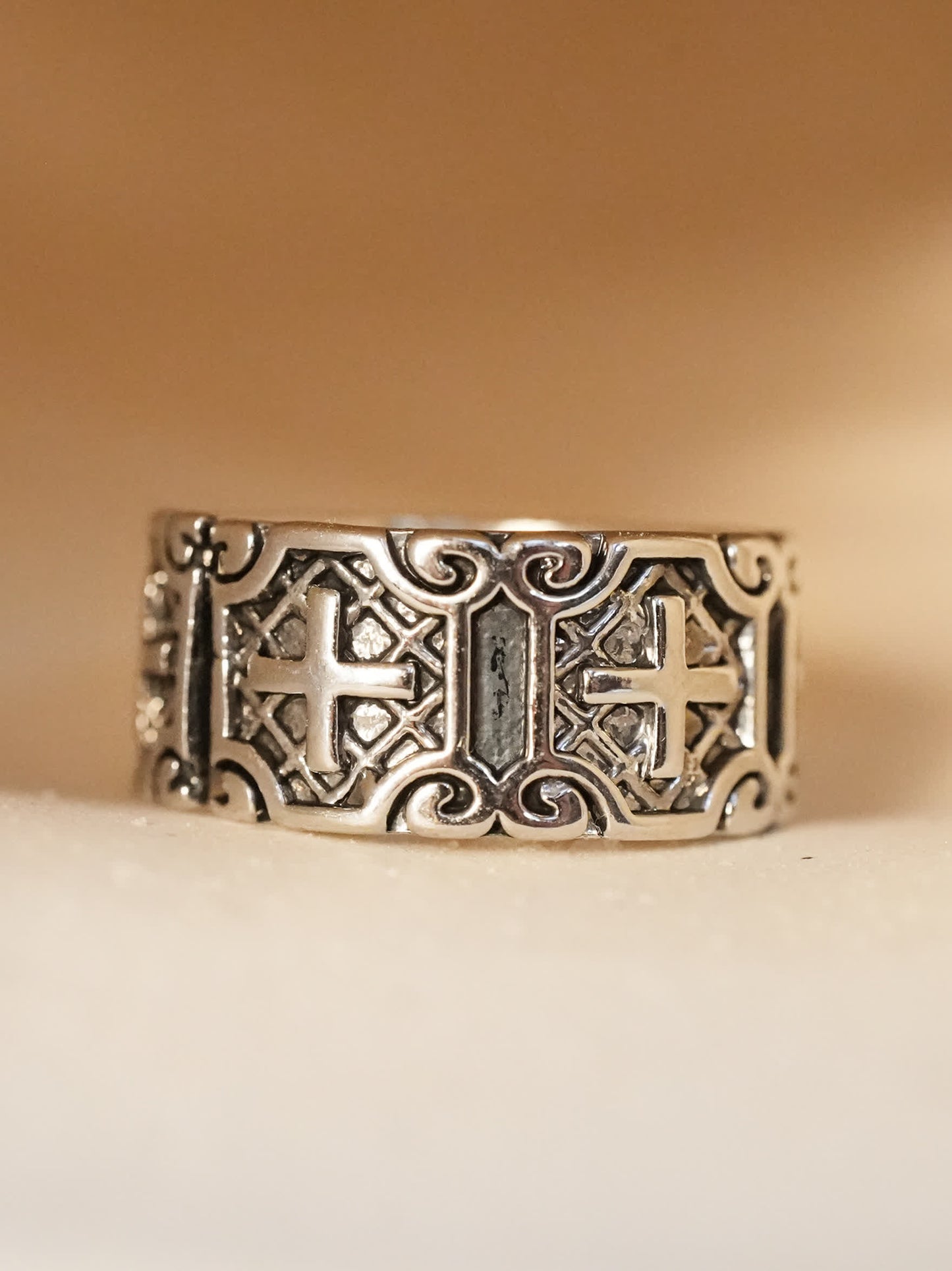 Brushed black and silver cross ring displayed on beige satin surface