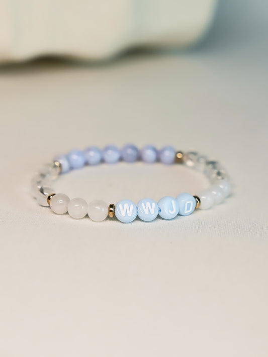 Angled product shot of the Quiet Steps WWJD Bracelet on a soft white background, highlighting the contrast between pastel gemstone beads and bold WWJD lettering.