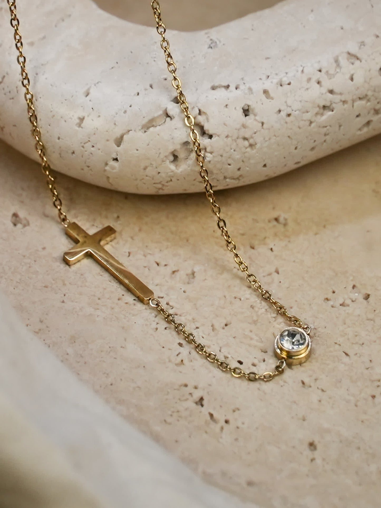 Minimalist sideways cross necklace displayed on neutral travertine surface
