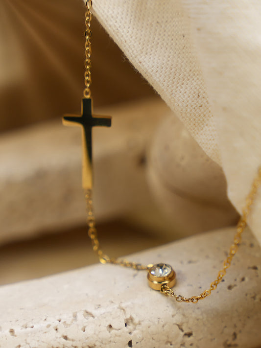 Close-up of gold sideways cross and cubic zirconia pendant resting on stone