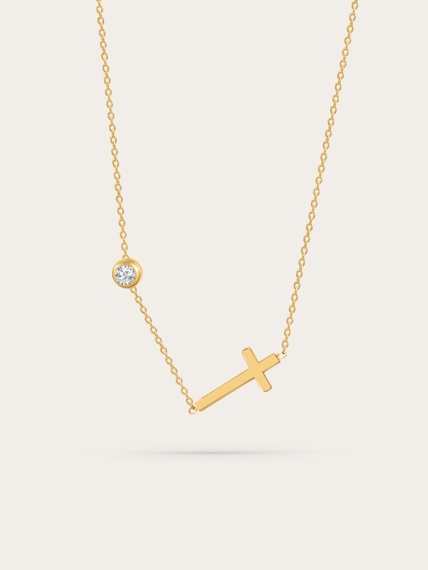 Sideways cross gold necklace with bezel-set zircon on light background