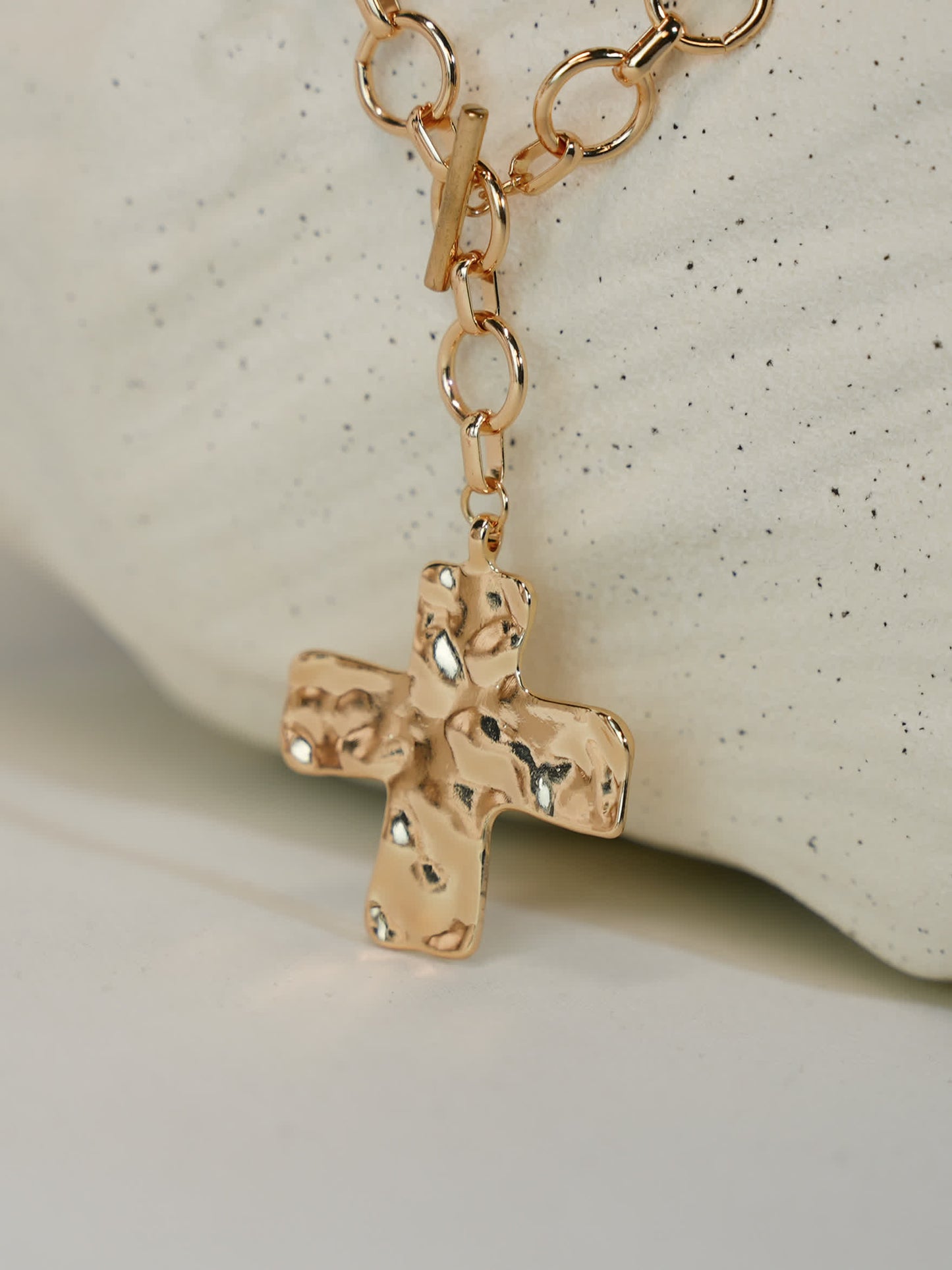 Close-up of hammered gold cross pendant with toggle clasp on minimalist display stone