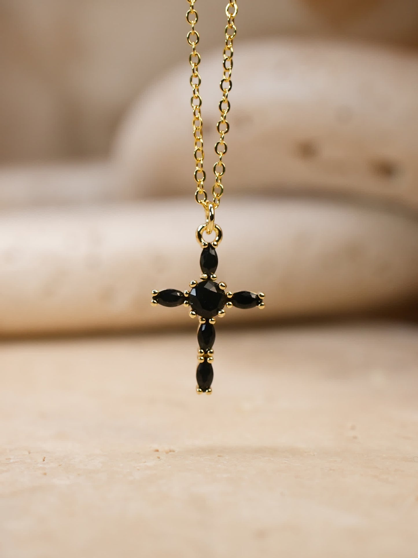 Front-facing image of black and gold cross necklace suspended over travertine surface